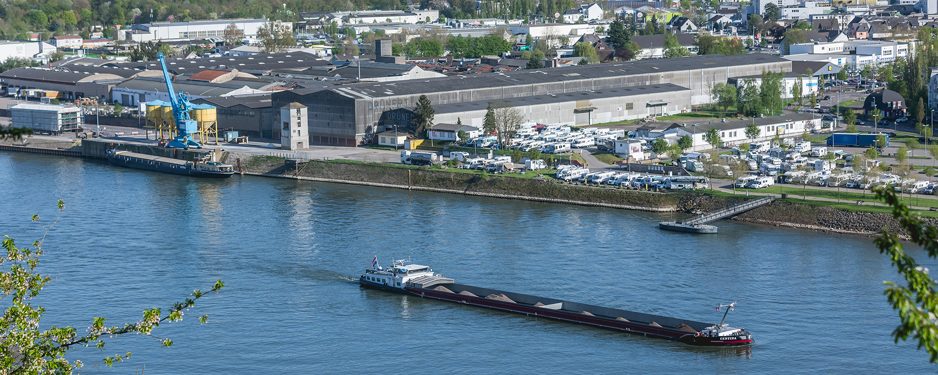 Das Bild zeigt ein Frachtschiff im Rhein bei Andernach, im Hintergrund sieht man den Andernacher Hafen.